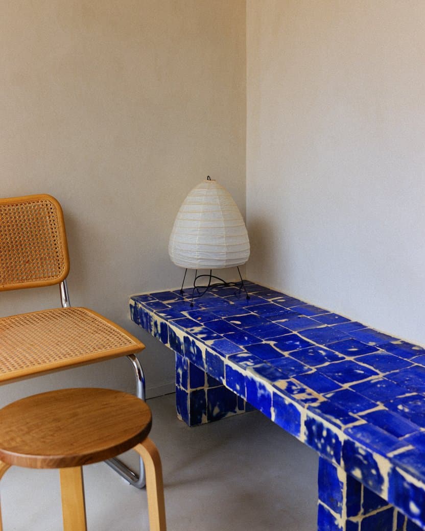 A low cobalt zellige bench in a white living corner with tubular steel furniture — after